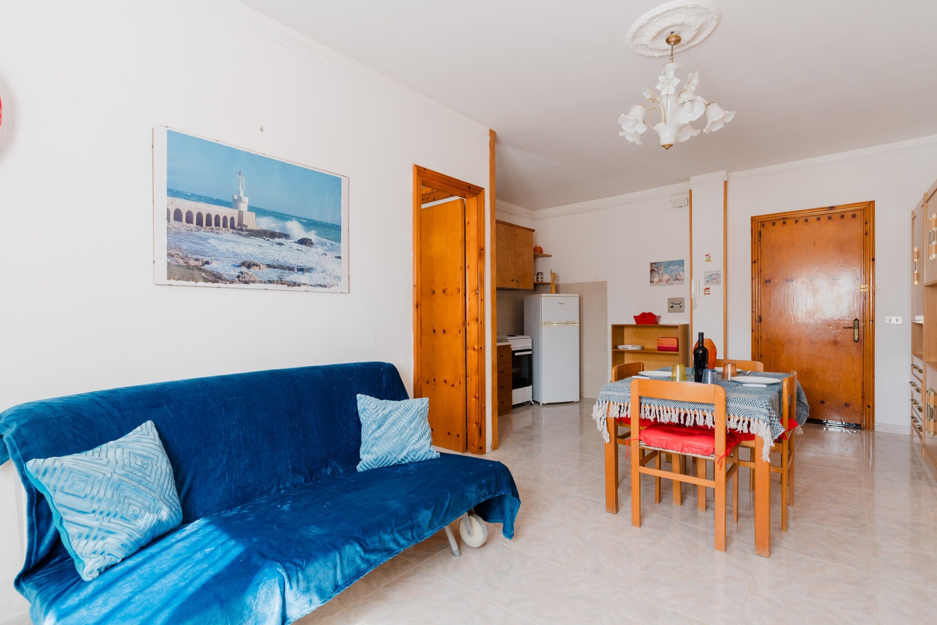 Una habitación con un sofá azul, una mesa de comedor con sillas, una zona de cocina y una puerta de madera.