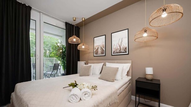 A bedroom with a bed, two wall-mounted wicker lamps, a bedside table with a lamp, and two framed pictures.