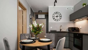 A modern kitchen with a clock, a dining table with chairs, and a vase with flowers.