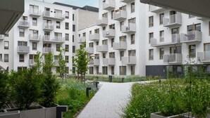 A modern apartment building with balconies, a central pathway, and surrounding greenery.