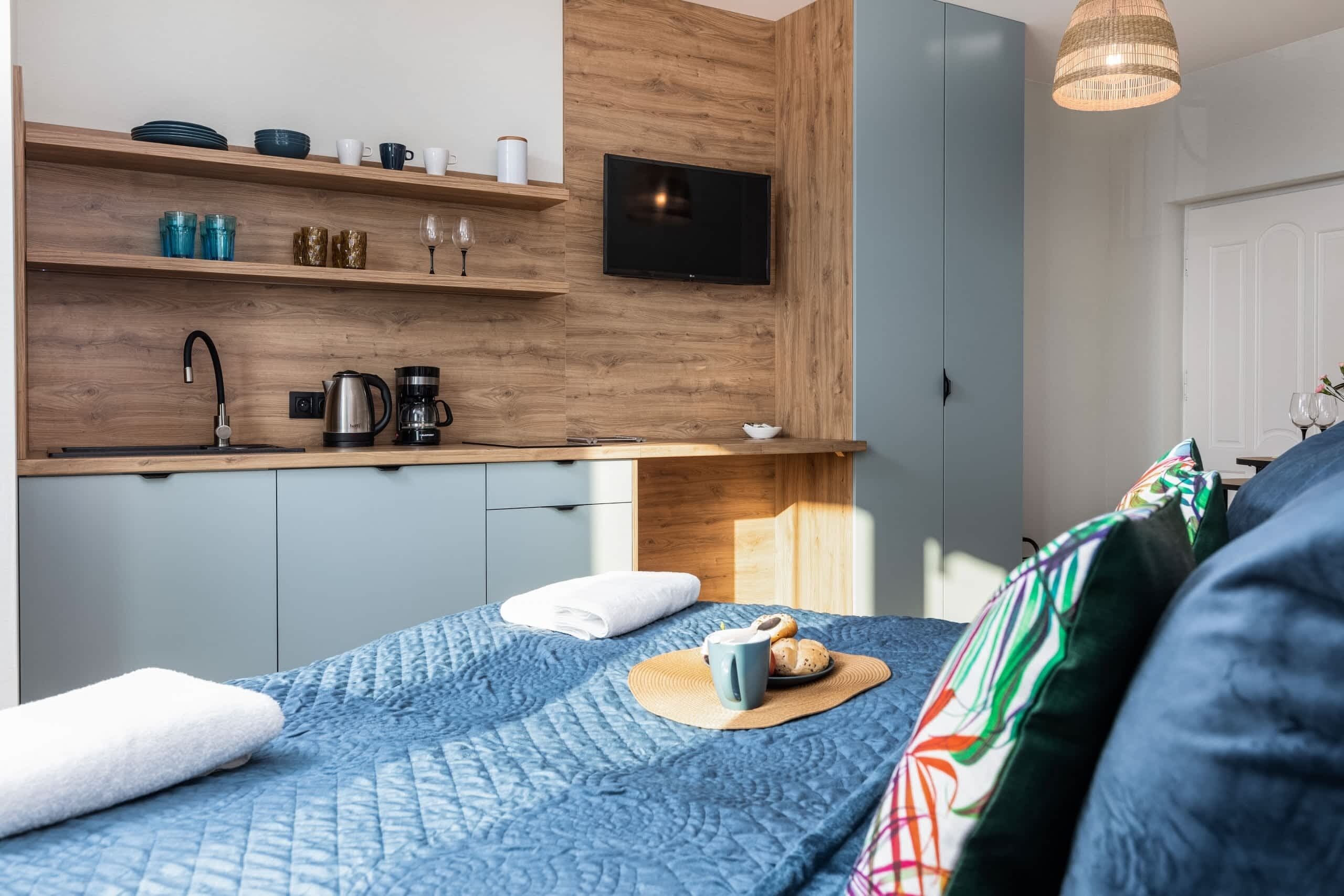 Ein gemütlicher Raum mit Bett, einer Küchenzeile mit Fernseher und einer Pendelleuchte.