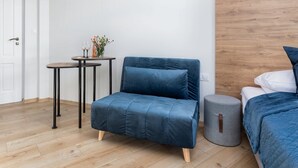 Una habitación moderna con un sofá azul, un otomanillo redondo, piso de madera y una cama con ropa de cama azul.