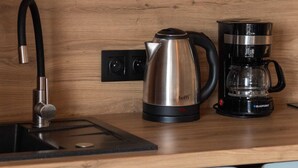 Una cocina con un lavamanos, un hervidor, una cafetera y cristalería sobre la encimera.