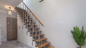 Un escalier moderne avec des marches en bois et des rampes en métal, menant à une pièce dotée d’une porte en bois et d’une plante en pot.