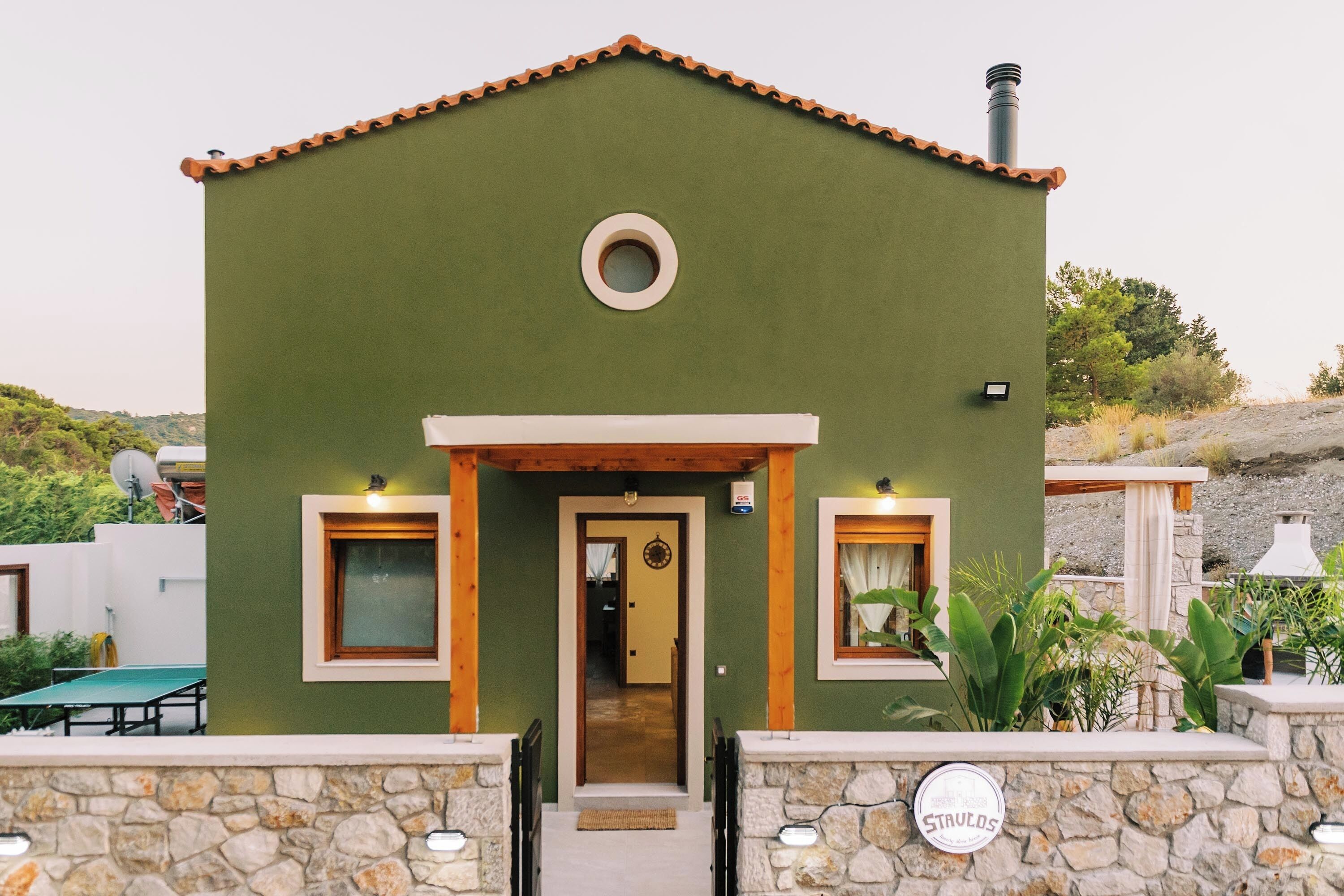 Un edificio verde con techo de tejas, una ventana circular y una puerta. Hay dos ventanas pequeñas a cada lado de la puerta.