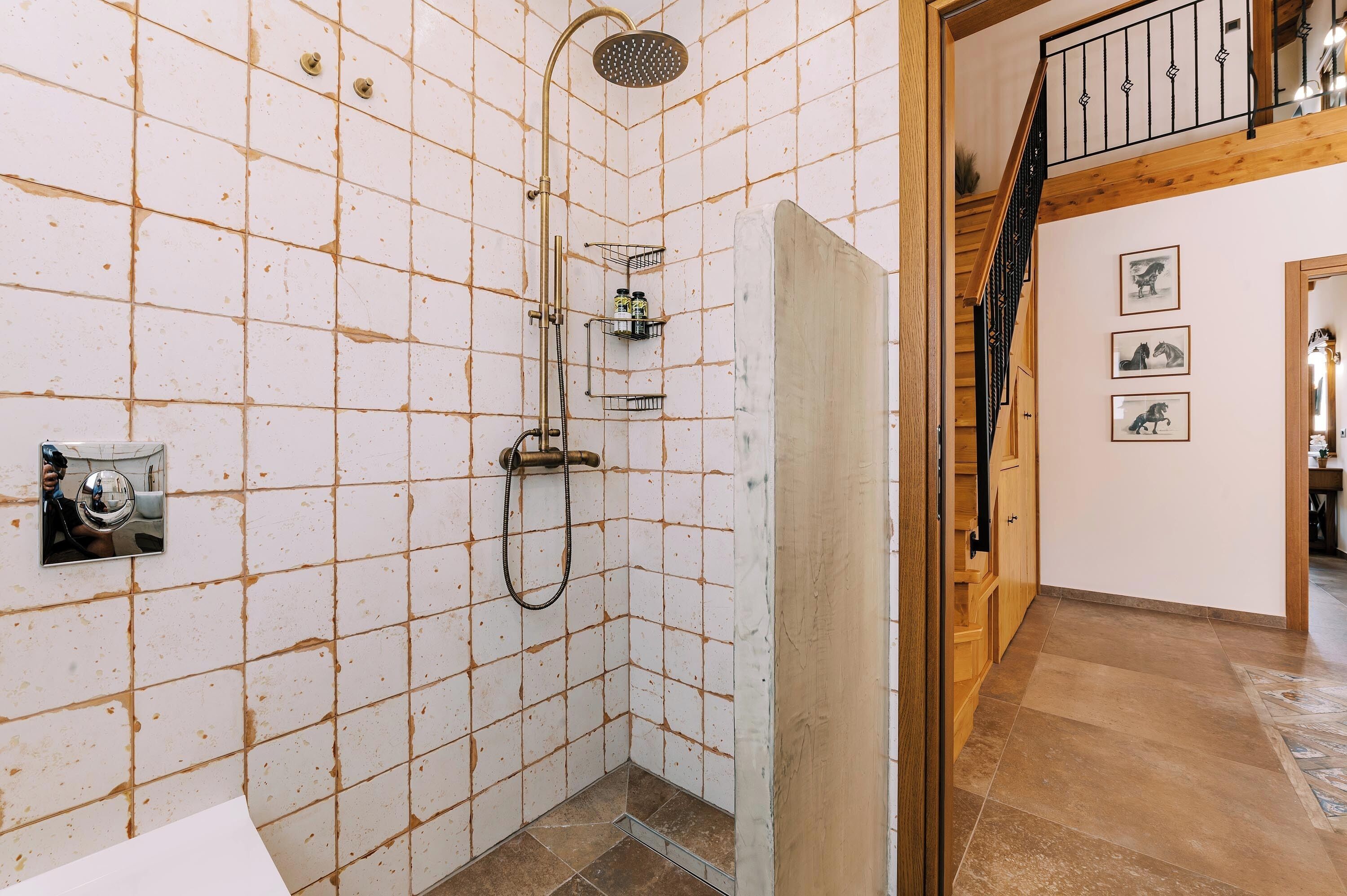 Un baño con paredes de azulejos blancos, una ducha y una escalera de madera.