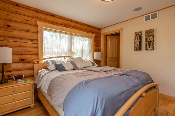A wooden cabin-style bedroom with a bed, nightstands, and a window with curtains.