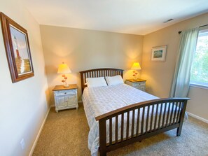 Une chambre à coucher comprenant un lit, deux tables de chevet, une commode, une fenêtre avec des rideaux et un tableau accroché au mur.