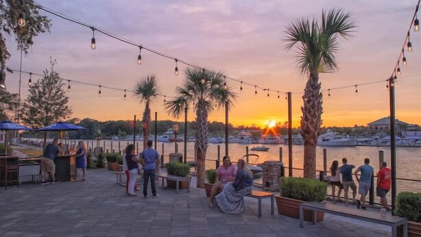 An outdoor patio area with string lights, palm trees, and a view of the sunset over a marina. - 3 bedroom house in Crescent Beach. Pets/motorcycles allowed. (North Myrtle Beach)