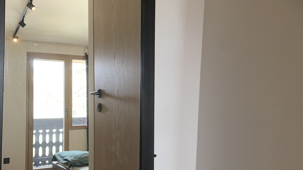 Una stanza con una porta di legno, un letto e vista su un balcone con ringhiera.
