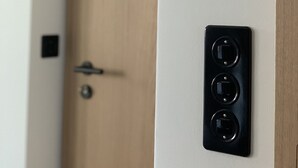 Una porta con pannello in legno e un dispositivo nero fissato al muro, dotato di tre pulsanti circolari.