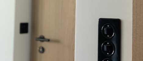 En dörr med en träpanel och en svart, väggmonterad apparat med tre runda knappar.