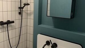 Un bagno con un lavandino bianco, uno specchio e una doccia con un tubo nero.