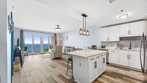 A modern kitchen with a central island, white cabinetry, and a view of the ocean through the sliding glass doors.