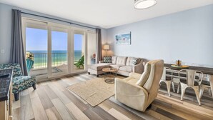 A spacious living room with a large sliding glass door leading to a balcony with a view of the ocean.