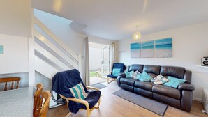 Een woonkamer met een leren bank, houten stoelen, een eettafel en uitzicht op de omgeving.