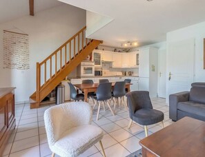 Ein modernes Wohnzimmer mit einer Couch, einem Couchtisch und einem Essbereich mit einem Holztisch und Stühlen. Eine Treppe führt zum Küchenbereich.