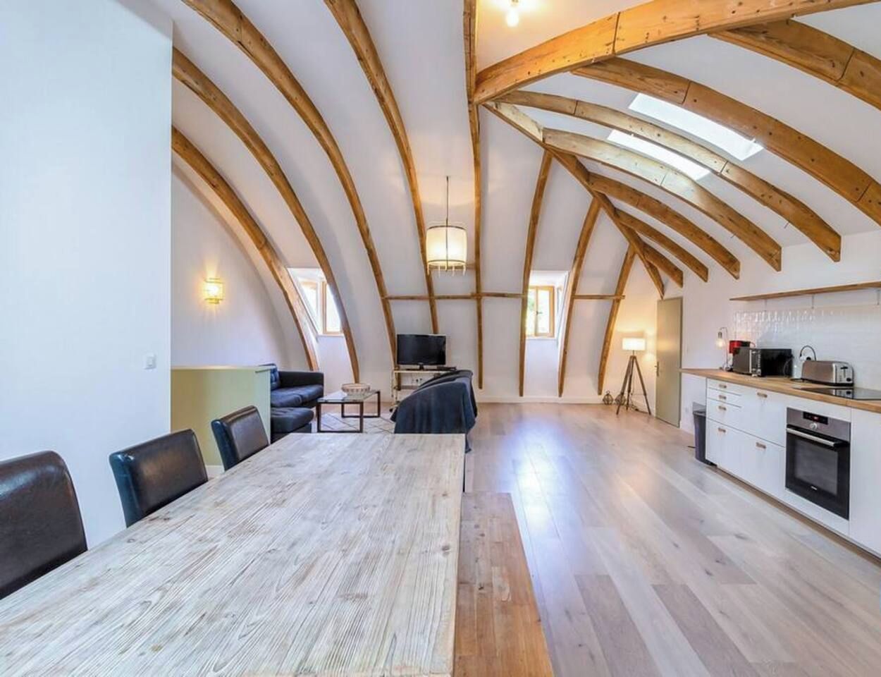 Un loft spacieux avec de hauts plafonds, des poutres apparentes, un coin repas, une cuisine et un téléviseur.
