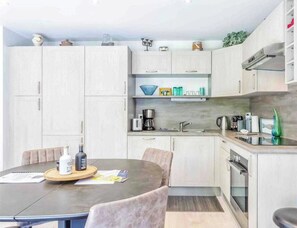A modern kitchen with light wood cabinets, a central island with seating, a built-in oven, and a coffee station.