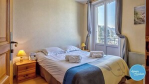 Ein Schlafzimmer mit Bett, Nachttischlampen, einem Fenster mit Vorhängen und Blick ins Freie.