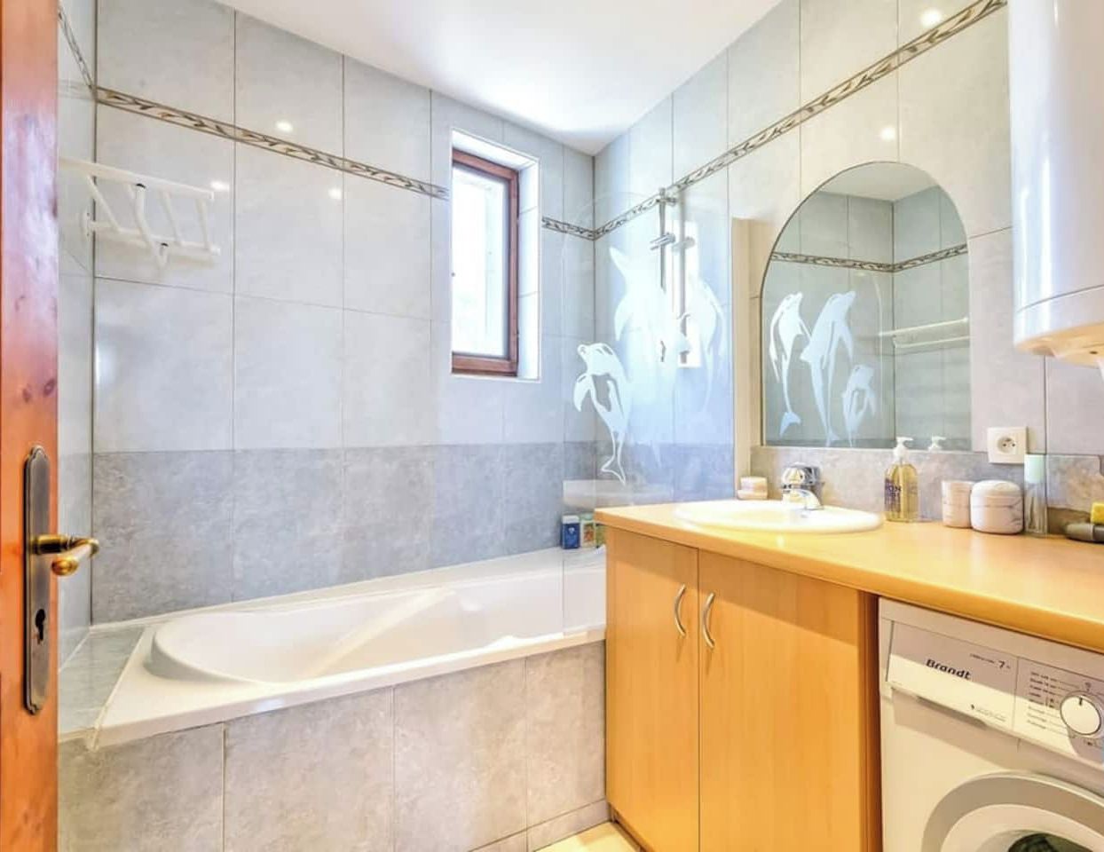 Une salle de bain moderne équipée d’une baignoire, d’un lavabo, d’un miroir et d’un lave-linge.
