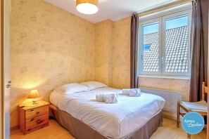 A bedroom with a bed, a nightstand, a lamp, and a window with curtains.