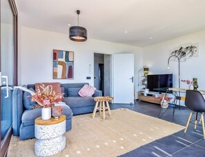 Una sala de estar moderna con un sofá gris, una mesa de centro, un televisor y una zona de comedor con una mesa y sillas.