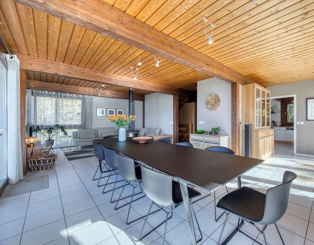 A spacious kitchen with a long island, modern chairs, and a dining area with a view of the outdoors.