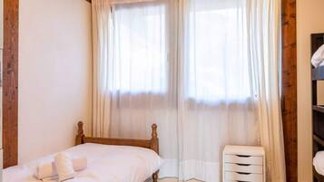 Ein Schlafzimmer mit einem hölzernen Bett, einem kleinen Nachttisch, einem Etagenbett und einem Fenster mit transparenten Vorhängen.