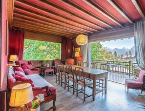 Une pièce chaleureuse avec un plafond en bois, une table à manger avec des chaises, un canapé et une vue sur un paysage montagneux grâce à de grandes fenêtres.