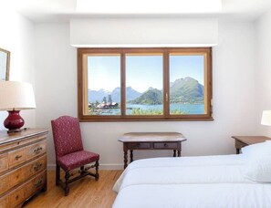 Une chambre à coucher comprenant un lit, une chaise, une petite table, une commode et une fenêtre donnant sur la montagne.