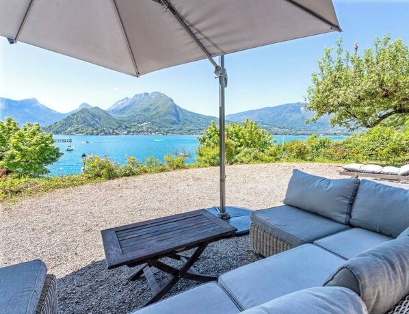 Une terrasse avec un canapé, une table et un parasol, d’où l’on peut admirer un lac avec des montagnes en arrière-plan.