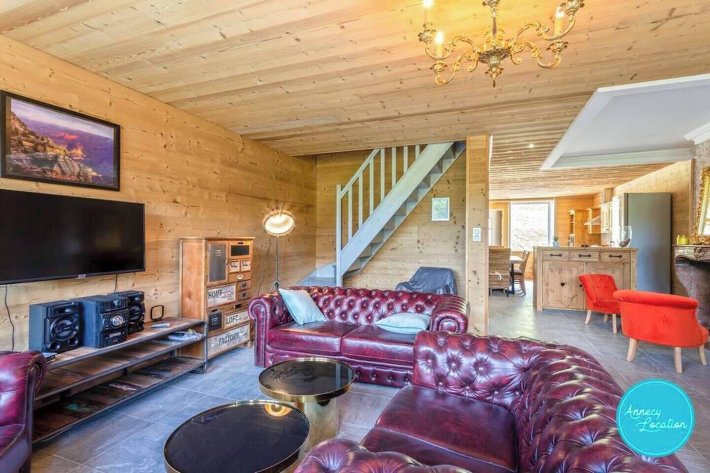 A cozy living room with a red leather sofa, a flat-screen TV, and a staircase leading to another room.