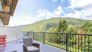 Ein Balkon mit Korbmöbeln und Blick auf einen bewaldeten Hügel.