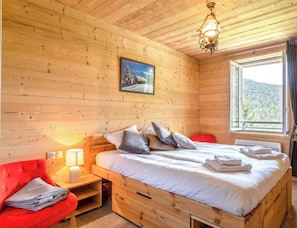 Une chambre à coucher dans une cabane en bois, avec un lit, une chaise rouge, une table de chevet avec une lampe et une fenêtre donnant sur l’extérieur.