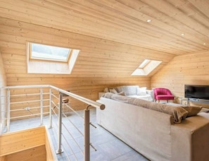 Een gezellig loft slaapkamer met houten plafond, een slaapbank, een roze stoel, een televisie en een trap met metalen leuning.