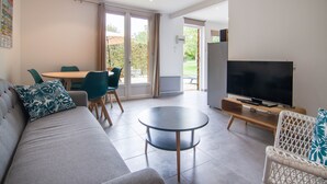 A modern living room with a sofa, a round coffee table, a TV, and a dining area with chairs and a table. - Suite Familiale - Le Clos Vallis (Sarlat-la-Canéda)
