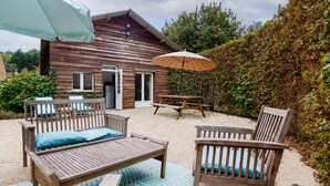A wooden cabin with a patio area featuring a table, chairs, and a bench. - Suite Familiale - Le Clos Vallis (Sarlat-la-Canéda)