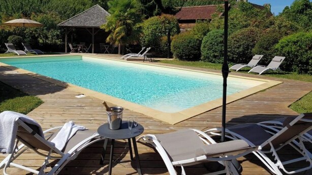A swimming pool with lounge chairs and umbrellas, surrounded by greenery. - Suite Familiale - Le Clos Vallis (Sarlat-la-Canéda)