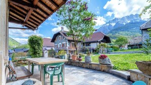 Eine Terrasse mit Tisch und Stühlen, Blumentöpfen und Blick auf Häuser und Berge.