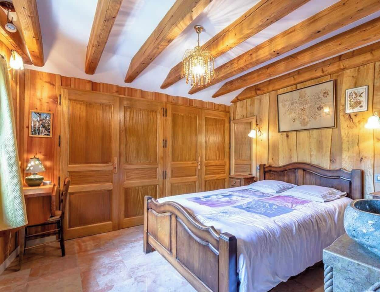 A wooden bedroom with a bed, a desk, and a stone basin.