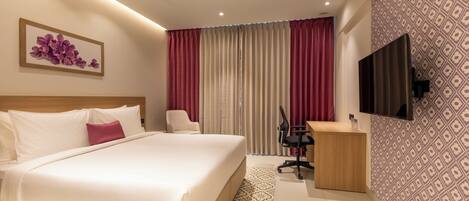 Habitación de hotel con cama, escritorio, silla, televisor y un papel tapiz estampado.