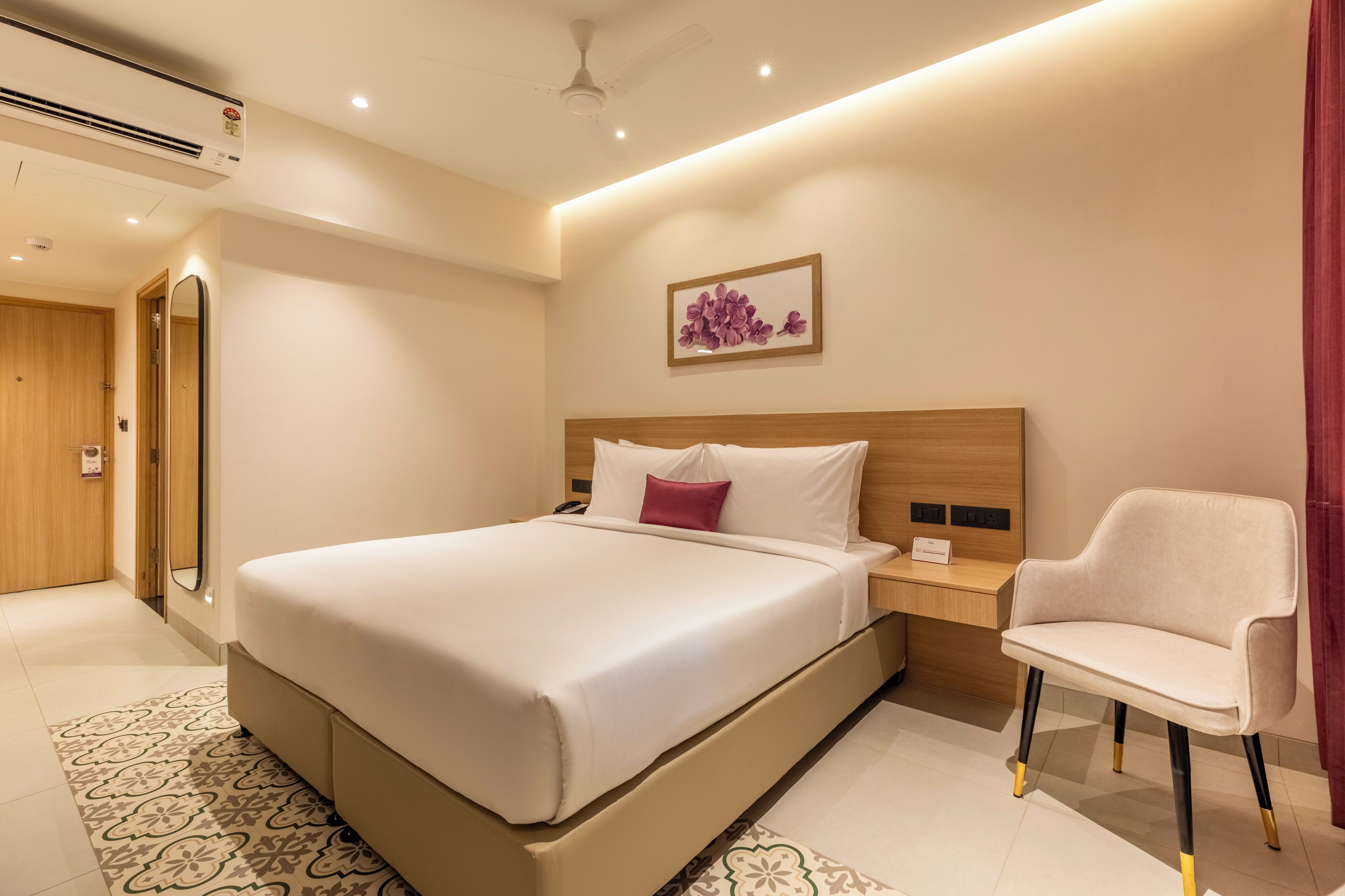 Habitación de hotel con una cama grande, mesita de noche, silla y una obra de arte en la pared.