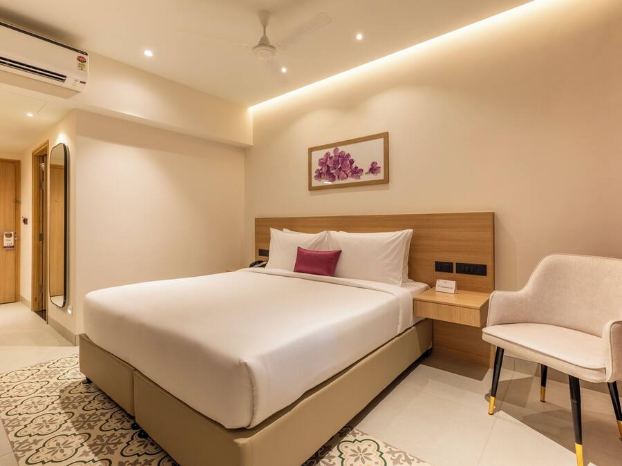 Habitación de hotel con una cama grande, mesita de noche, silla y una obra de arte en la pared.