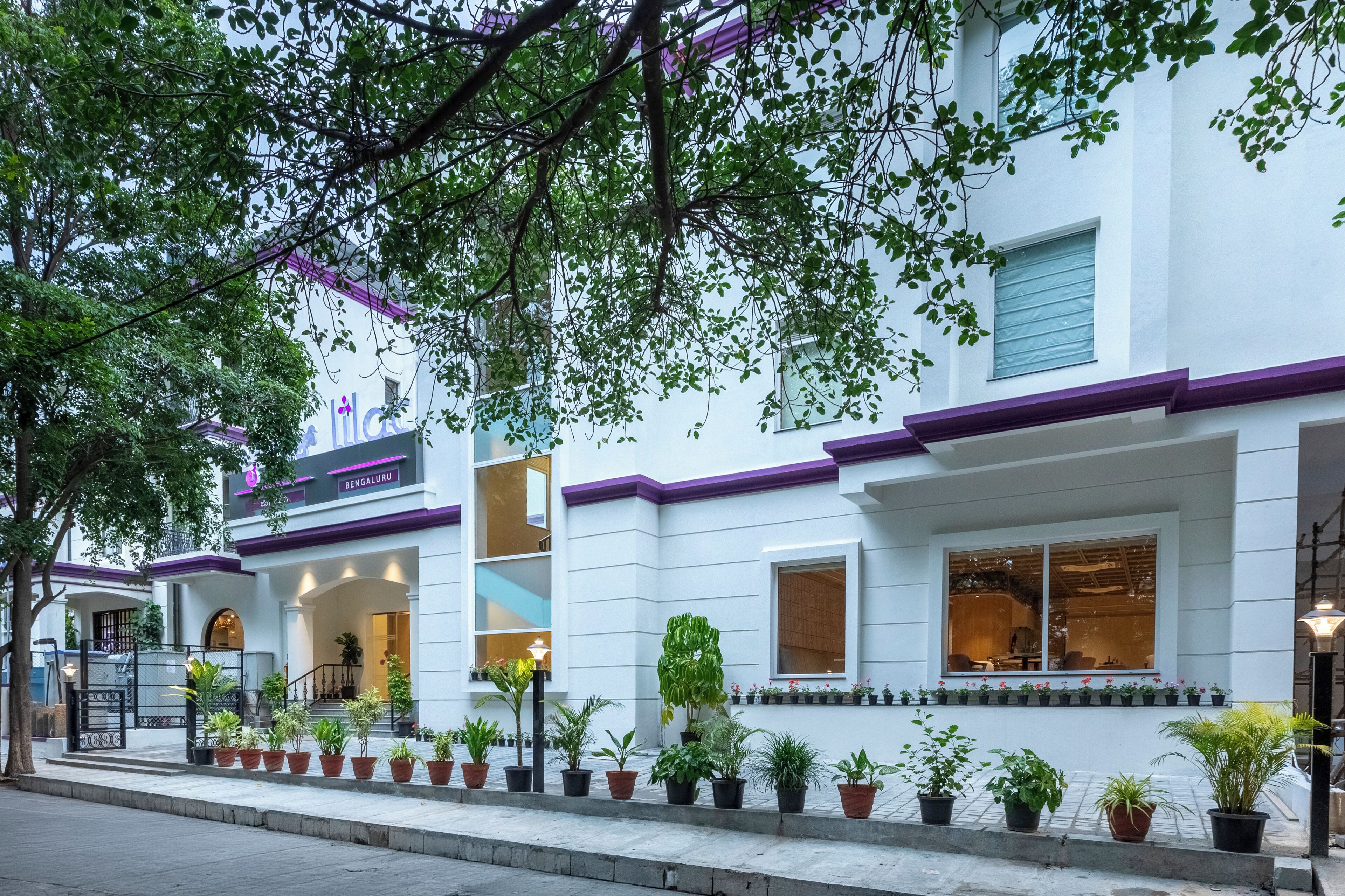 A hotel with a white facade and purple trim, featuring a signboard with the name 'Lilac' and 'Bengaluru' on it.