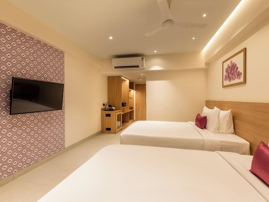 Quarto de hotel com duas camas, uma televisão presa na parede, um aparelho de ar condicionado e um quadro pendurado na parede.