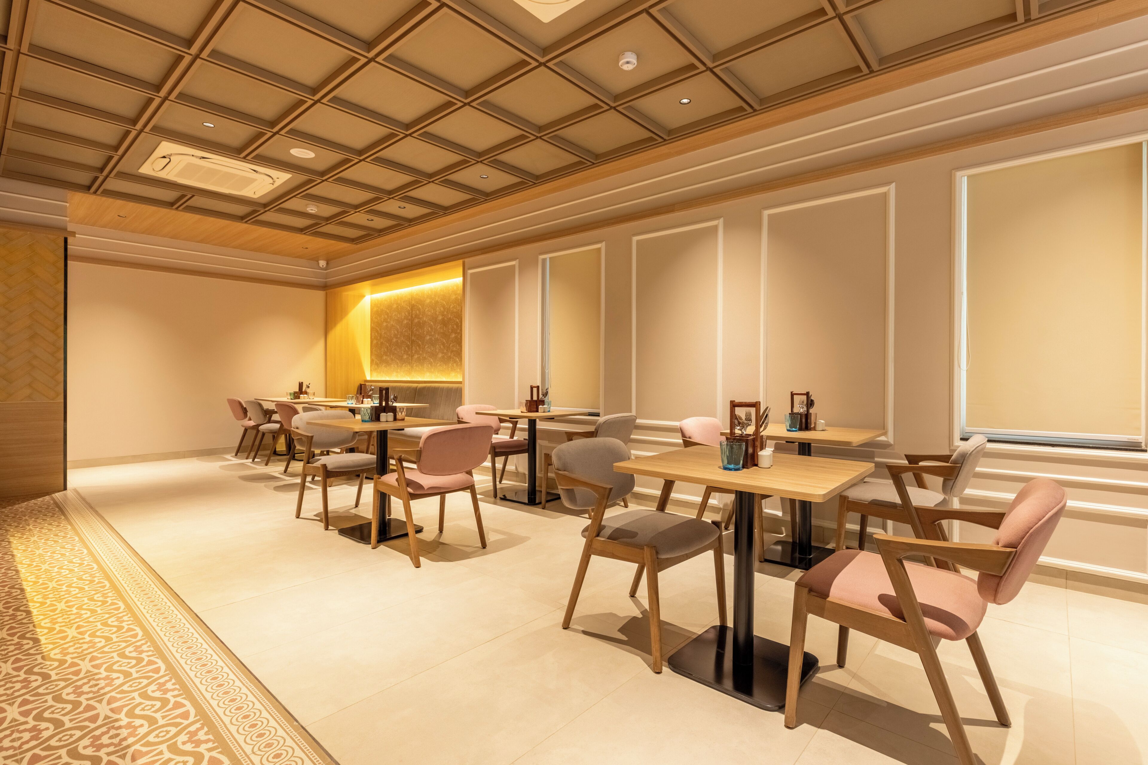 Un comedor de hotel con mesas y sillas, un suelo estampado e iluminación empotrada en el techo.