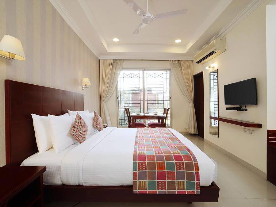Habitación de hotel con una cama grande, televisor montado en la pared, ventilador de techo y ventana con cortinas.