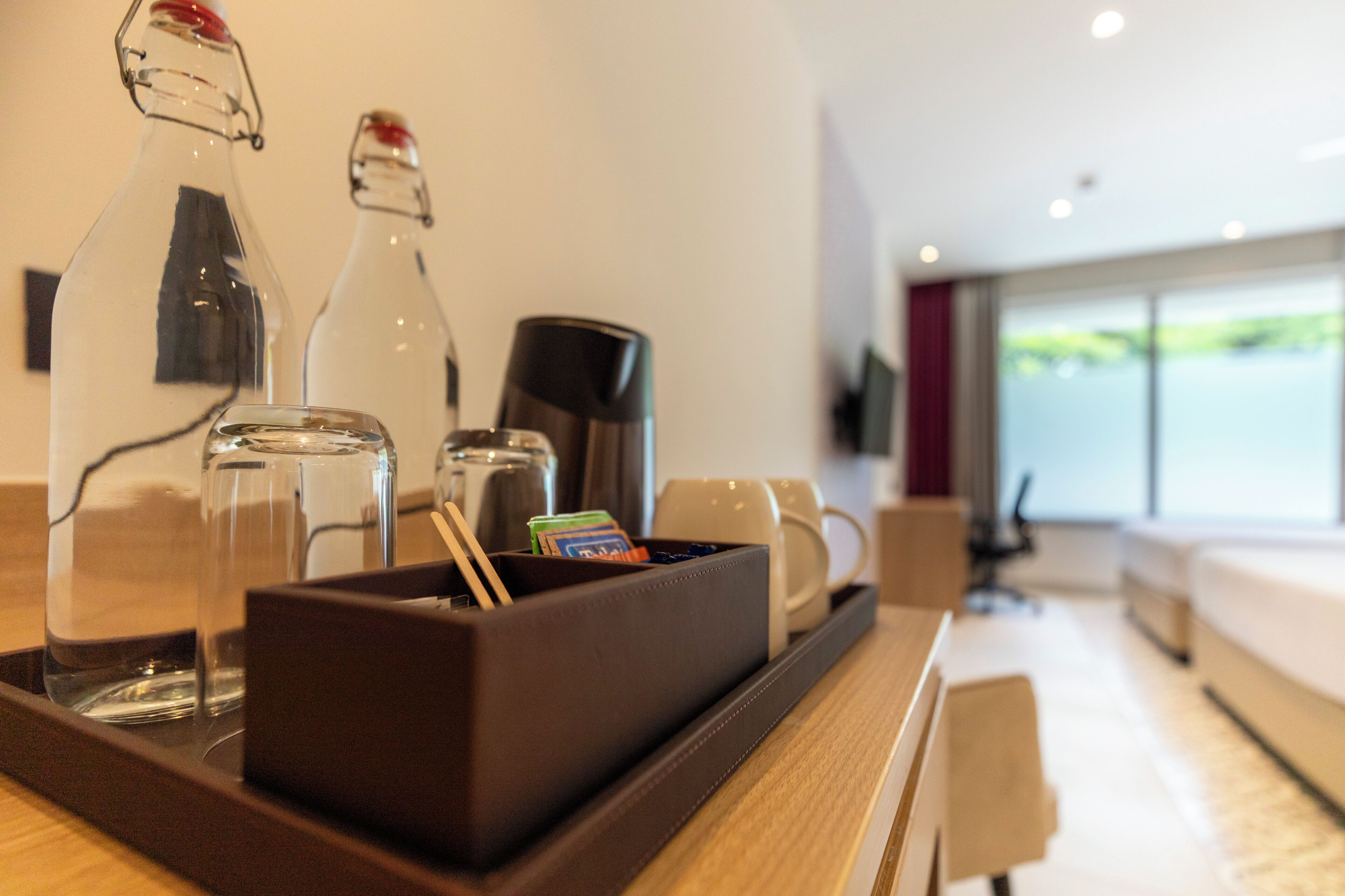 A hotel room with a breakfast tray containing a bottle, a glass, a coffee maker, and a box with cards.