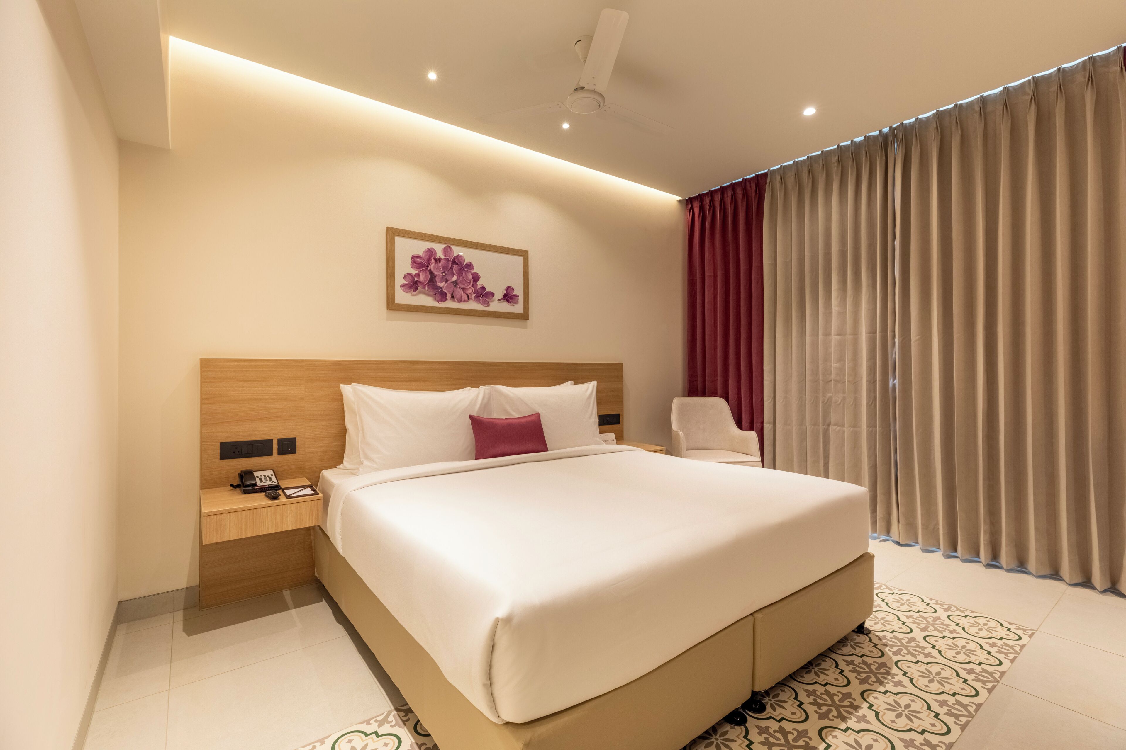 A hotel room with a large bed, a bedside table with a phone, a chair, and a window with curtains.